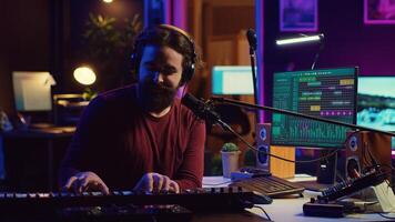 Musician playing piano midi controller and recording a new song, singing on microphone in his home studio. Sound engineer working on digital audio workstation, using electronic keyboard. Camera A. photo