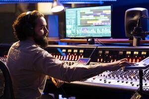 Sound engineer working in professional studio to mix and master tracks, expert editing music in control room. Audio technician using faders and knobs on dashboard, technical equipment. photo
