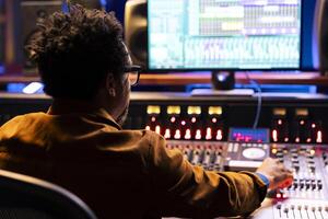 Sound engineer uses mixing console and handling panel board buttons, pushing sliders in control room for adjusting volume levels. Technician creates music in professional music studio. photo