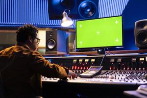 Audio technician uses computer with isolated layout and control panel board, professional music studio. Producer recording tracks and editing with sliders or buttons, control room gear. photo