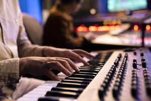 Artist performer recording his song on electronic keyboard piano, working with audio engineer in professional studio and producing new music. Singer composes on synthesizer. Close up. photo