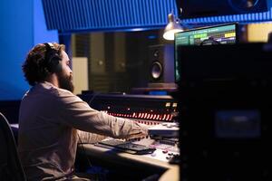 Music producer customizes and edits songs to generate new tunes, adding sound effects to refine rhythm on recordings. Professional technician in audio engineering works in control room. photo