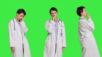Tired general practitioner yawning and feeling overworked after night shift at hospital, exhaustion and work pressure. Medic being tired and experiencing burnout against greenscreen. Camera B. photo