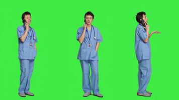 Health specialist using smartphone to make important calls, standing against greenscreen backdrop. Nurse talking to patients for checkup exams on telephone line, calling people to confirm. Camera A. photo
