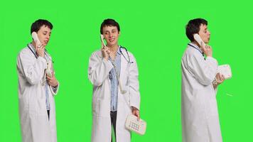Physician answering landline phone call against greenscreen backdrop, talking to patients about checkup appointments. Medic having remote discussion on retro telephone with cord. Camera B. photo