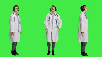 Joyful physician dancing around in the studio with music on headset, having fun with modern cool songs against greenscreen backdrop. Medic woman enjoying audio tunes and singing. Camera A. photo