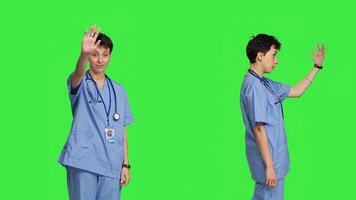 Medical assistant calling people over to come closer for examination, inviting patients at cabinet for checkup. Nurse with scrubs stands against greenscreen, come at me concept. Camera B. photo