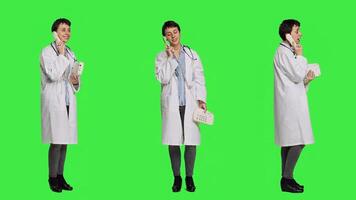 Physician answering landline phone call against greenscreen backdrop, talking to patients about checkup appointments. Medic having remote discussion on retro telephone with cord. Camera A. photo