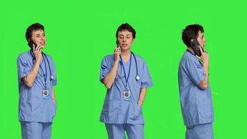 Health specialist using smartphone to make important calls, standing against greenscreen backdrop. Nurse talking to patients for checkup exams on telephone line, calling people to confirm. Camera B. photo