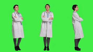 Portrait of successful physician standing with arms crossed against greenscreen backdrop, wearing a white coat and stethoscope. Doctor feeling confident with healthcare expertise. Camera A. photo