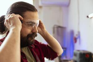 Carpenter in woodworking shop putting on protection glasses before assembling furniture. Cabinetmaker preparing safety equipment in joinery before starting work, close up shot photo