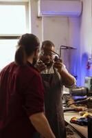 Master in carpentry shop instructing BIPOC worker to wear protection gear, preventing workplace accidents. Cabinetmaker making sure apprentice uses safety earmuffs and goggles to avoid injury photo