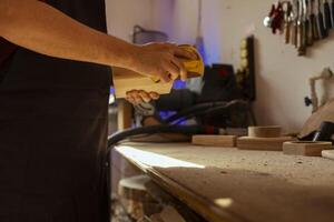 Man working in assembly shop using sanding block to remove imperfections on wood piece. Carpenter using coarse grade sandpaper to do manual sanding, employed in furniture assembly workspace photo