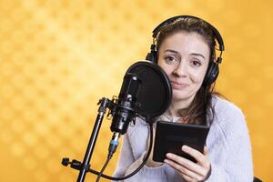 Smiling woman doing voiceover word for word reading of ebook on ereader to produce digital audiobook. Happy voice actor using storytelling skills while reading text from tablet, recording novel photo