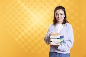 Portrait of woman holding stack of books needed for her education, isolated over studio background. Person using pile of textbooks for knowledge acquisition during academic learning photo