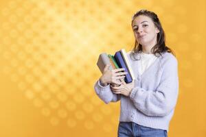 Portrait of smiling woman holding stack of books in arms, isolated over studio background. Happy student using pile of textbooks for knowledge acquisition during academic learning photo