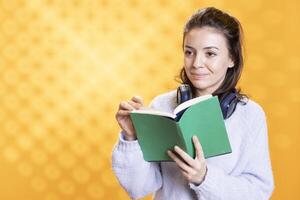 Smiling woman browsing through book pages, enjoying literature, having fun, isolated over studio background. Cheerful person reading novel, relaxing and enjoying leisure time photo