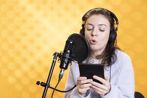 Voice actor reading ebook from ereader, recording for audiobook production using microphone, isolated over studio background. Woman using mic to produce digital recording of novel from text on tablet photo
