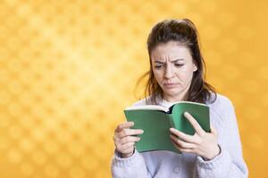Woman frowns seeing length of lecture book needed for school exam, studio background. Student glares at difficult academic textbook needed to pass classes, feeling troubled and stressed while reading photo