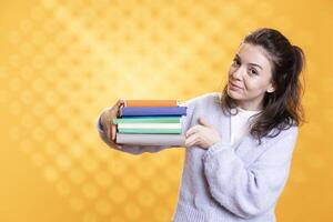 Portrait of upbeat woman holding pile of books, recommending reading, studio background. Radiant person with stack of novels showcasing importance of appreciation for literature photo