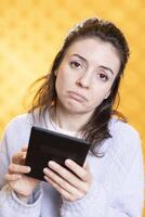 Portrait of upset woman reading difficult book for school exam on tablet, studio background. Student pouting, feeling sad while researching for university homework using digital device photo