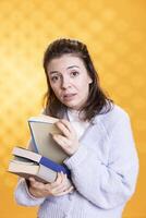 Portrait of woman searching through stack of books in frenzy to gather information for school exam, studio background. Student nervous before university assessment, rushing to find necessary textbook photo