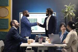Business partners celebrate the starting point of a project between their firms, shaking hands in meeting. Administrators forging agreement to develop enterprise internationally and collect funds. photo