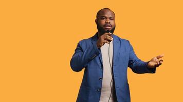 Portrait of african american lecturer holding monologue using microphone, gesturing with hands, studio background. Expressive BIPOC speaker talking during presentation using mic, camera B photo