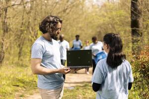 Team of ecology volunteers using pc with greenscreen in the woods, gathering to collect trash and plant trees for future generations. Environmental conservation of the natural habitat. photo