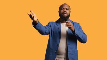 African american motivational speaker holding monologue using microphone, gesturing with hands, studio background. Energetic BIPOC speaker talking during presentation using mic, doing speech, camera B photo