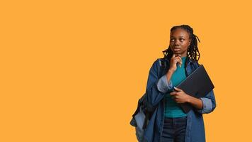 Pensive woman carrying laptop, doing thinking gesture, memorizing information for school exam, studio background. Student holding notebook, remembering before university assessment, camera B photo