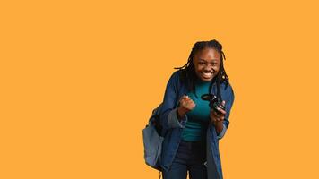 Euphoric african american woman playing intense gaming console game, celebrating win, studio background. Ecstatic young girl using controller, excited after being victorious in videogame, camera B photo