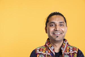 Portrait of jolly friendly indian man smiling, looking pleased, isolated over studio background. Joyful expressive asian person in traditional attire grinning, feeling satisfied photo