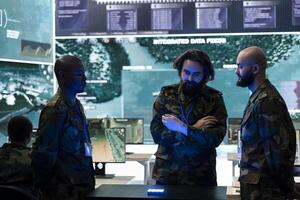 Diverse soldiers analyzing satellite images on a 3d hologram to discuss operations plan in command post, operating with high tech gear. Recruits using 3d projection for new defense mission. photo