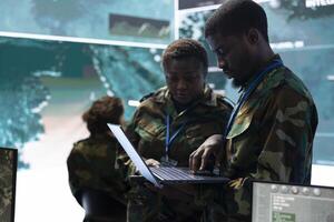 Team of army conscripts collecting important information from military radar surveillance system, working in command room power base of operations. National safety operations. photo