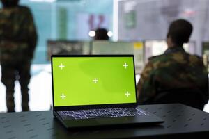 Laptop showing isolated green screen in military power base, federal defense personnel working on collecting real time information for a new operation. Military headquarters with high tech. photo