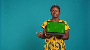 Confident happy person posing with a copy space mockup on laptop, create an advertisement with isolated display in studio. Young woman in ethnic attire with floral elements. Camera B. photo
