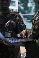 Diverse army staff collecting real time data on a laptop in control room, communicating important information for the infantry unit operations. IT engineers working in command center. Close up. photo