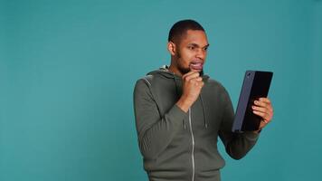 Angry man fighting with friend during videocall on tablet, isolated over studio background. Rude person in disagreement with mate, swearing and pointing finger in teleconference meeting, camera B photo