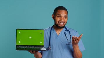 Portrait of practitioner in medical uniform showing instructions on isolated screen laptop. Healthcare professional doing presentation using mockup notebook, studio backdrop, camera A photo