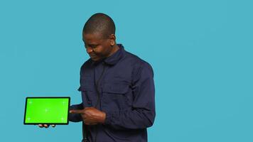 Portrait of security agent presenting chroma key tablet and securing assigned post, studio background. Guardian points finger to isolated screen device while handling security breaches, camera A photo