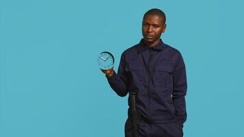 Security guard holding clock, rushing people out of property. Portrait of stern bodyguard showing visitors time is passing, preparing for closing down location, studio background, camera B photo