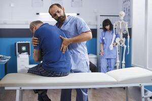 Osteopathic nurse gently extends spine of elderly patient with injury as part of physiotherapy. Chiropractor provides aid to gentleman experiencing back pains, aiding in physical recovery. photo