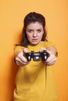 Portrait of focused woman in front of camera holding wireless controller. In studio, young female adult engaged in an online game, using joystick to play on console. photo