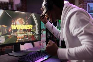 African american gamer ecstatic about winning online multiplayer match against enemies. Man seeing winner message on gaming PC computer display, shouting at screen from happiness photo