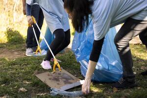 Child and woman grabbing junk and plastic from the ground, recycling in disposal bags and fighting the forest pollution. Volunteers team picking up trash and garbage to restore nature. photo