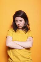 Woman standing in studio with crossed arms, disapproving and displeased facial expression on camera. Portrait of a dissatisfied person striking a grumpy and solemn expression. photo