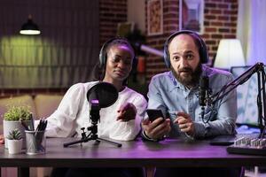 African american content creator and man during online show in neon lights studio, shooting vlog using professional microphones. Vloggers discussing with audience during live broadcast photo