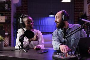 Experienced radio host playing music in professional on air studio, impressing african american guest showing thumbs up hand gesturing. Dj using high quality setup to stream musical production photo