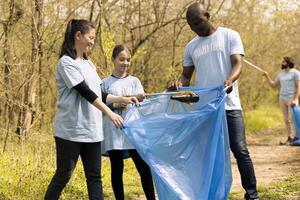 Group of environmentalists working to clean the forest from junk, collecting rubbish and plastic waste in bags. Young activists grabbing garbage and recycling, support ecological justice. photo